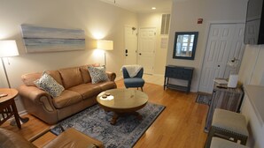 A living room with a brown leather sofa, a round glass coffee table, a blue armchair, and a wooden side table. - Creekwood Condo Close to Shopping, Dininng and Beaches! (Rehoboth Beach)