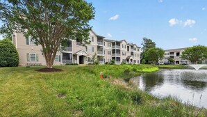 A residential building with multiple balconies, a pond, and a well-maintained lawn. - Creekwood Condo Close to Shopping, Dininng and Beaches! (Rehoboth Beach)