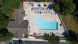 An aerial view of a property with a swimming pool surrounded by lounge chairs and tables, a parking area, and a fenced garden. - Creekwood Condo Close to Shopping, Dininng and Beaches! (Rehoboth Beach)