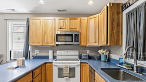 A kitchen with wooden cabinets, a microwave, a stove, a sink, and a window with curtains.