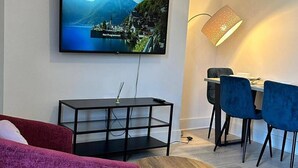 Moderni olohuone, jossa on televisio, ruokailutila tuoleineen, lamppu ja sohva.