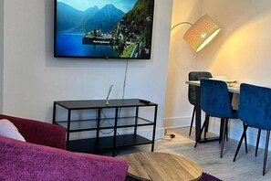 Una sala de estar moderna con televisor, comedor con sillas, lámpara y sofá.