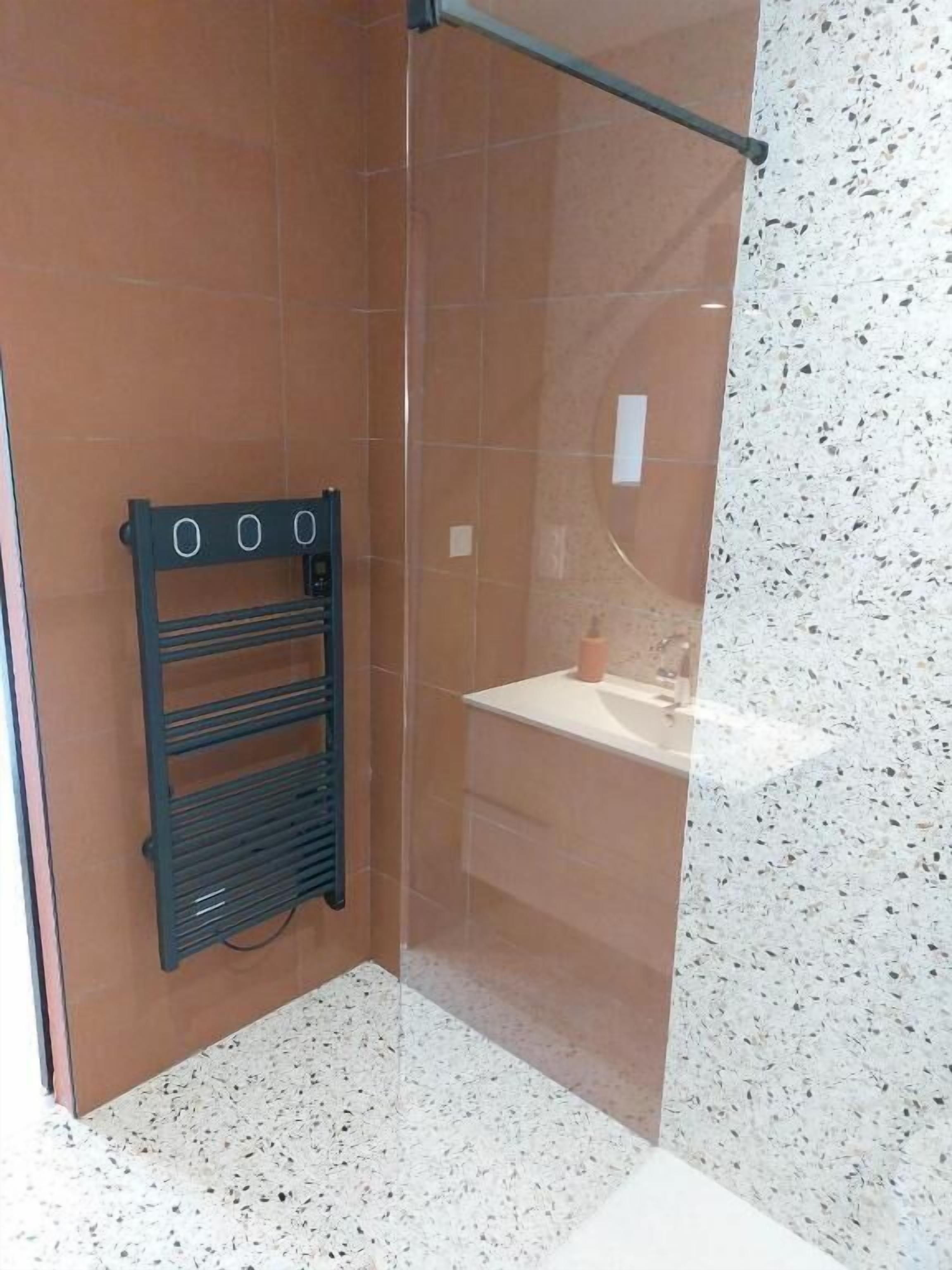 A shower with a glass door, a black towel rack, and a marble-tiled wall.