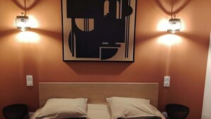 Una habitación de hotel con cama, dos lámparas de noche, una obra de arte en la pared y una manta roja.