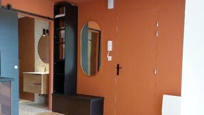 Una habitación con piso de madera, un espejo grande, una puerta y un radiador pequeño y blanco.