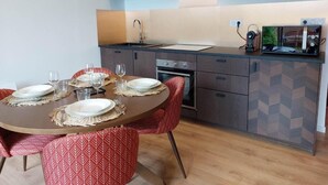 Una cocina moderna con armarios de madera, horno empotrado y comedor con una mesa redonda y sillas rojas con estampado.