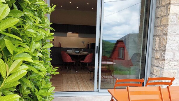 Un patio con terraza de madera, sillas naranjas y puerta de vidrio que da a un comedor interior.