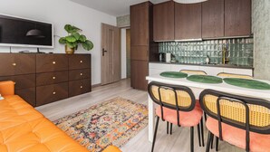 Una cocina moderna con armarios de madera, una mesa de comedor con sillas, un televisor y una planta.