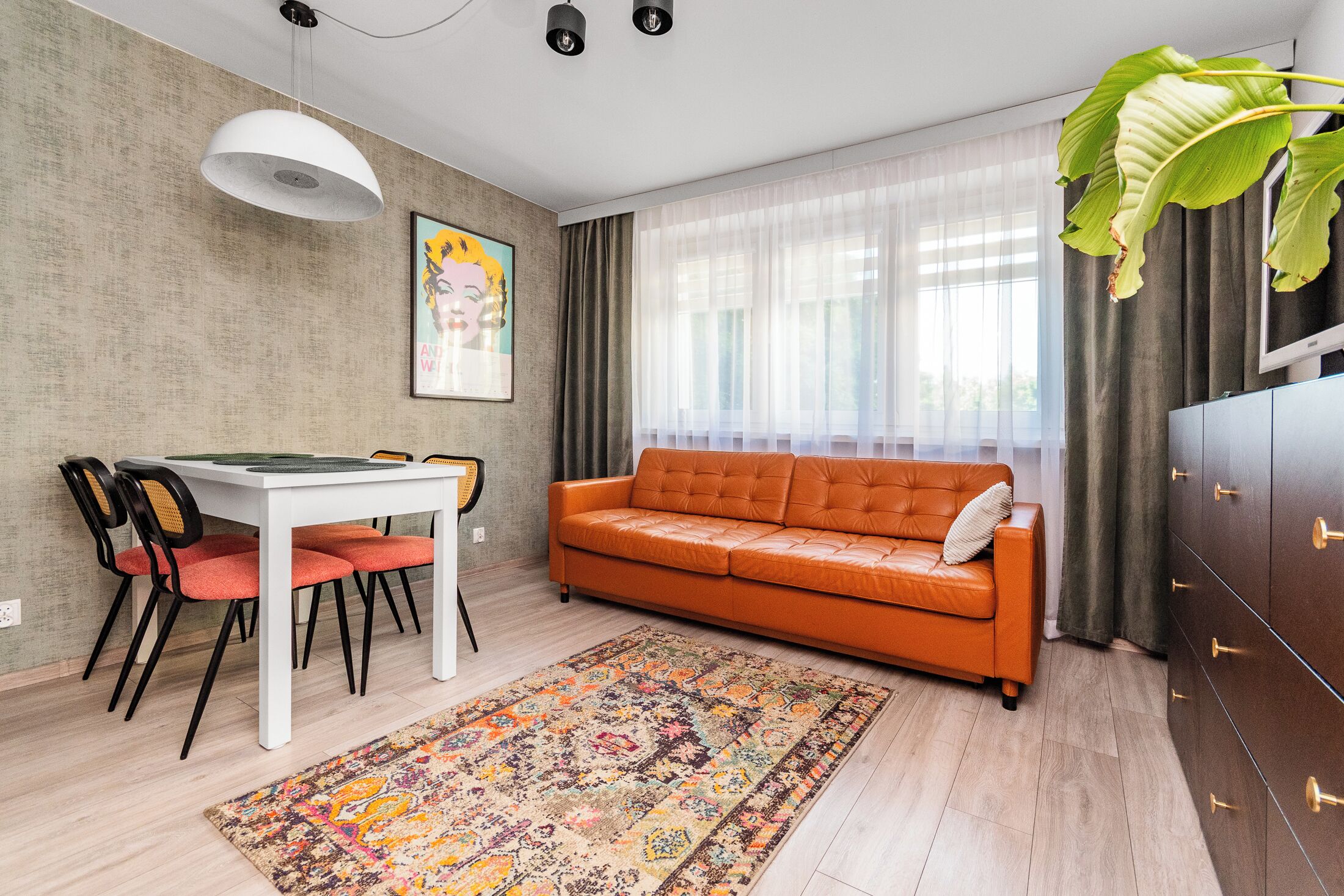 A modern living room with a dining table, orange sofa, and a large plant.