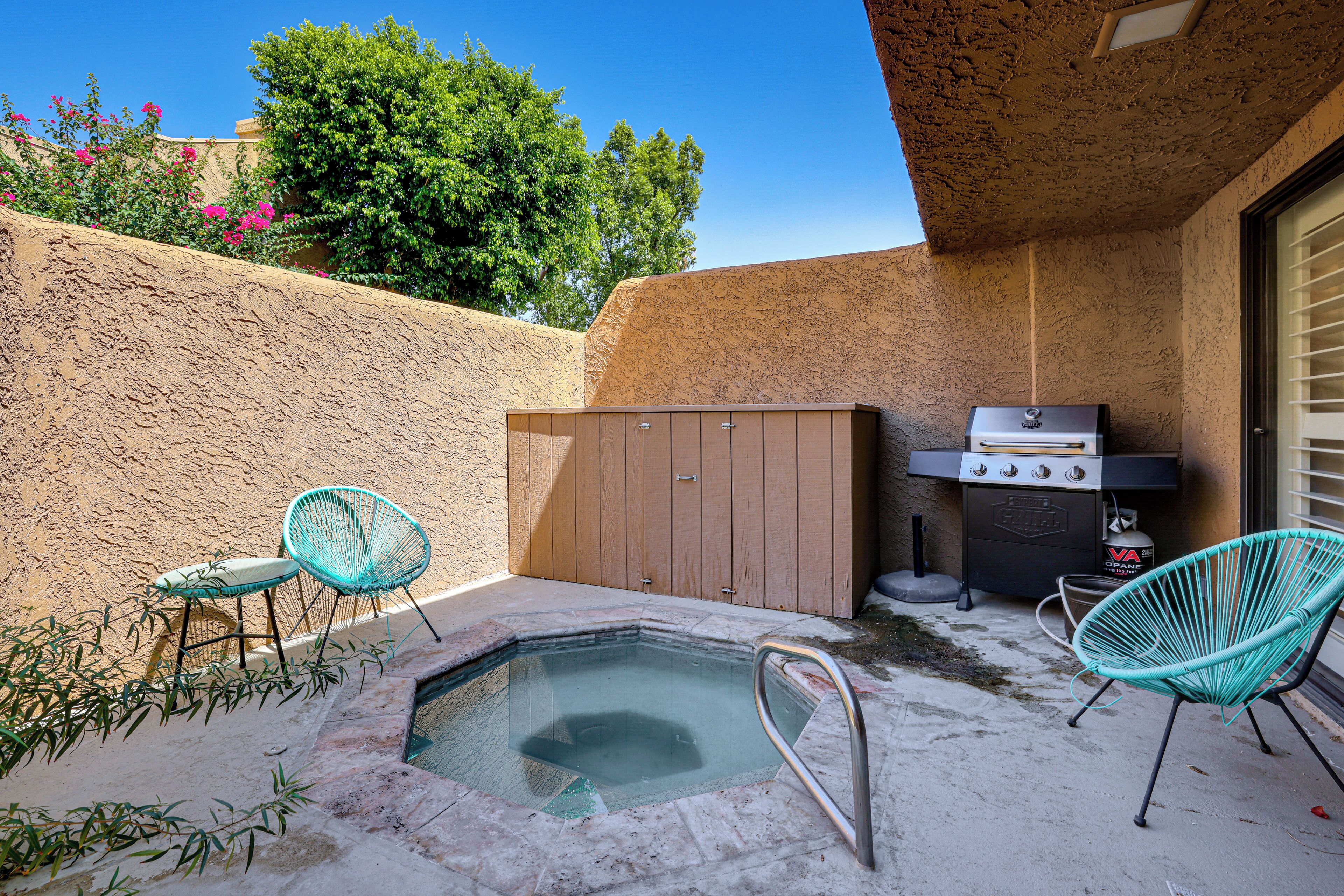 A backyard with a hot tub, two chairs, a barbecue grill, and a wooden shed.