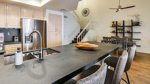 Uma cozinha moderna com ilha central, eletrodomésticos de aço inoxidável e um espaço de refeições com cadeiras e mesa.