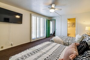 Ein Schlafzimmer mit zwei Betten, einem Deckenventilator, einem an der Wand montierten Fernseher und einer grünen Tür, die in einen anderen Raum führt.