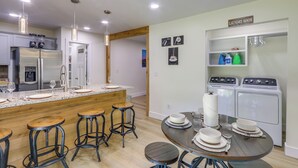 Cozinha moderna com uma ilha central, banquetas de bar, mesa de jantar posta com pratos e copos, e um rolo grande de papel toalha.