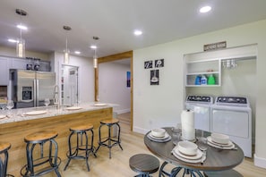 Una cocina moderna con una isla central, taburetes de bar, una mesa de comedor y un letrero que indica lavandería, así como una lavadora.