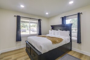 Ein Schlafzimmer mit Bett, einem Fenster mit Vorhängen, einer Deckenleuchte und Blick nach draußen.