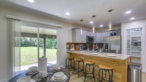 Uma cozinha moderna com ilha central, banquetas e vista para o exterior.
