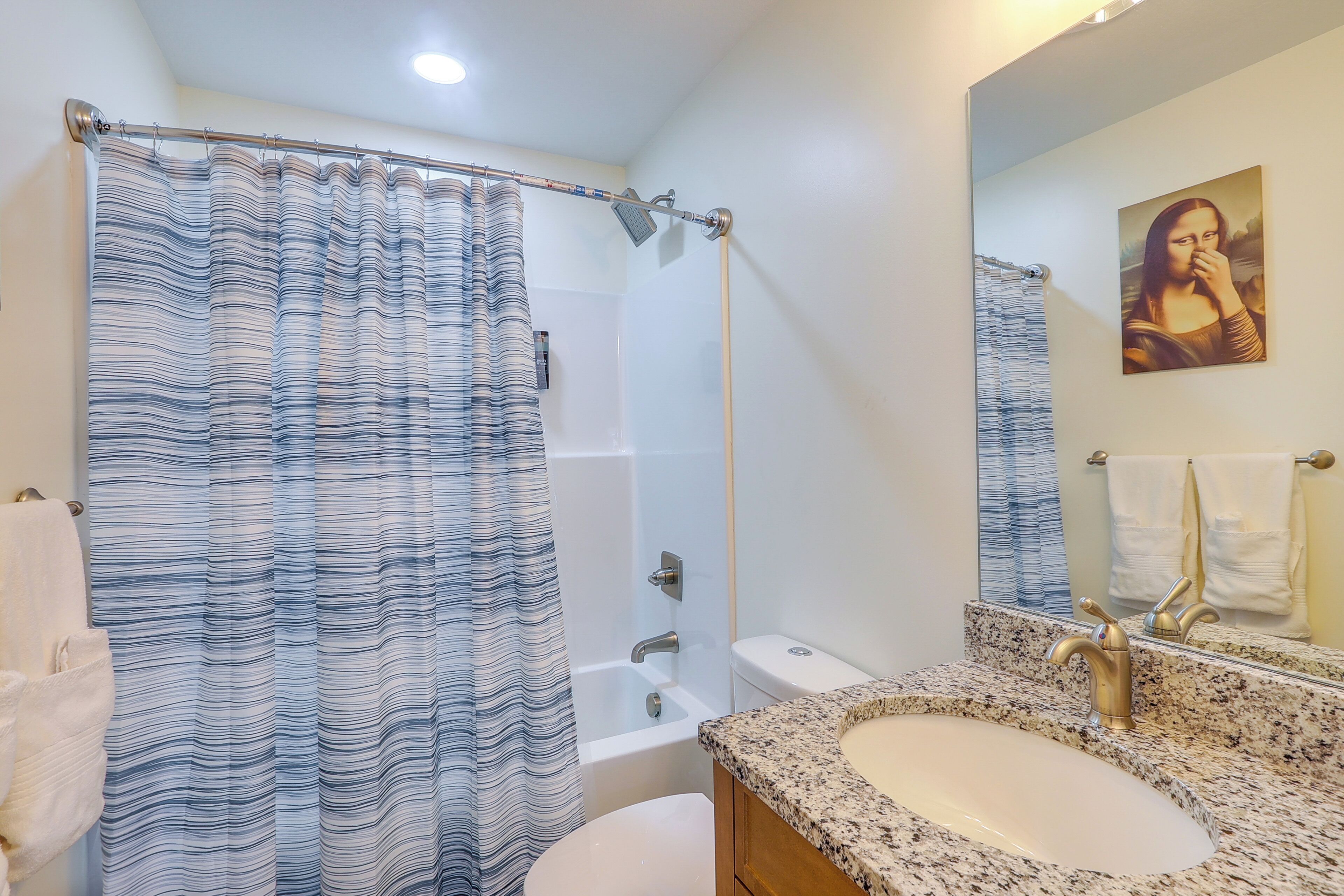 A bathroom with a shower curtain, bathtub, toilet, sink, and a mirror with a painting.
