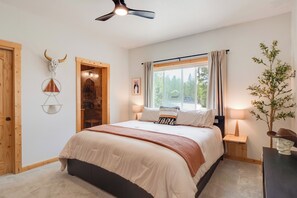 Ein Schlafzimmer mit einem Bett, Nachttischen, einem Deckenventilator, einem Fenster mit Vorhängen und einer Wanddekoration.