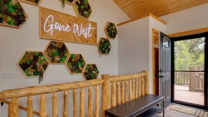 A wooden bench, a neon sign reading 'Gone West,' hexagonal planters with plants, and a door leading to an outdoor deck. - Rocky Mtn Hideaway w/ Hot Tub & Panoramic Views (Fairplay)