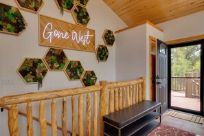 Eine Holzbank, ein leuchtendes Neon-Schild mit der Aufschrift 'Gone West', sechseckige Pflanzgefäße mit Bepflanzung und eine Tür zu einer Außenterrasse.