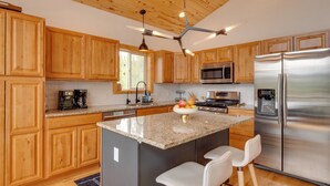 A modern kitchen with wooden cabinets, granite countertops, stainless steel appliances, and a central island with bar stools. - Rocky Mtn Hideaway w/ Hot Tub & Panoramic Views (Fairplay)