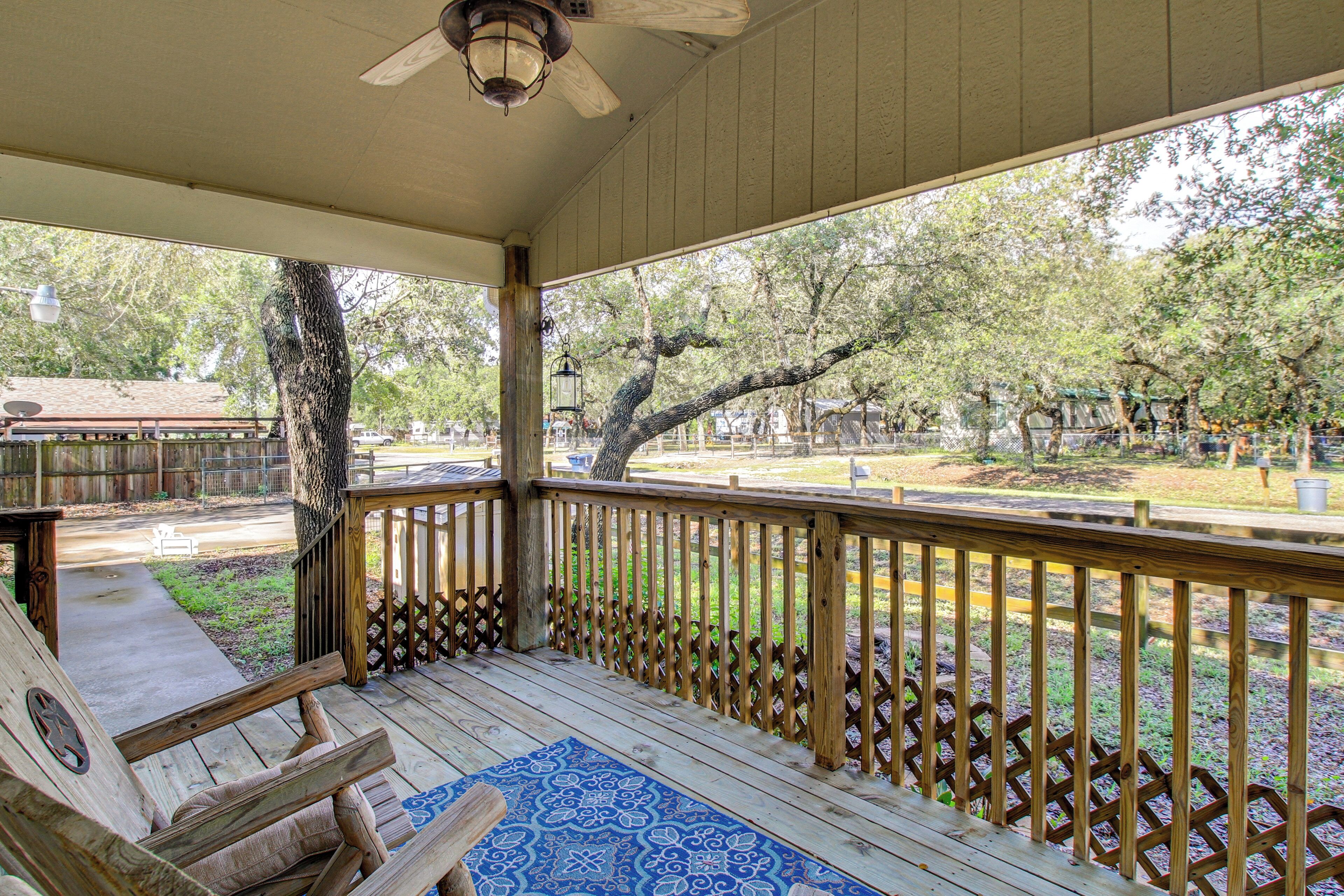 A wooden deck with a railing, a ceiling fan, and a patterned rug.