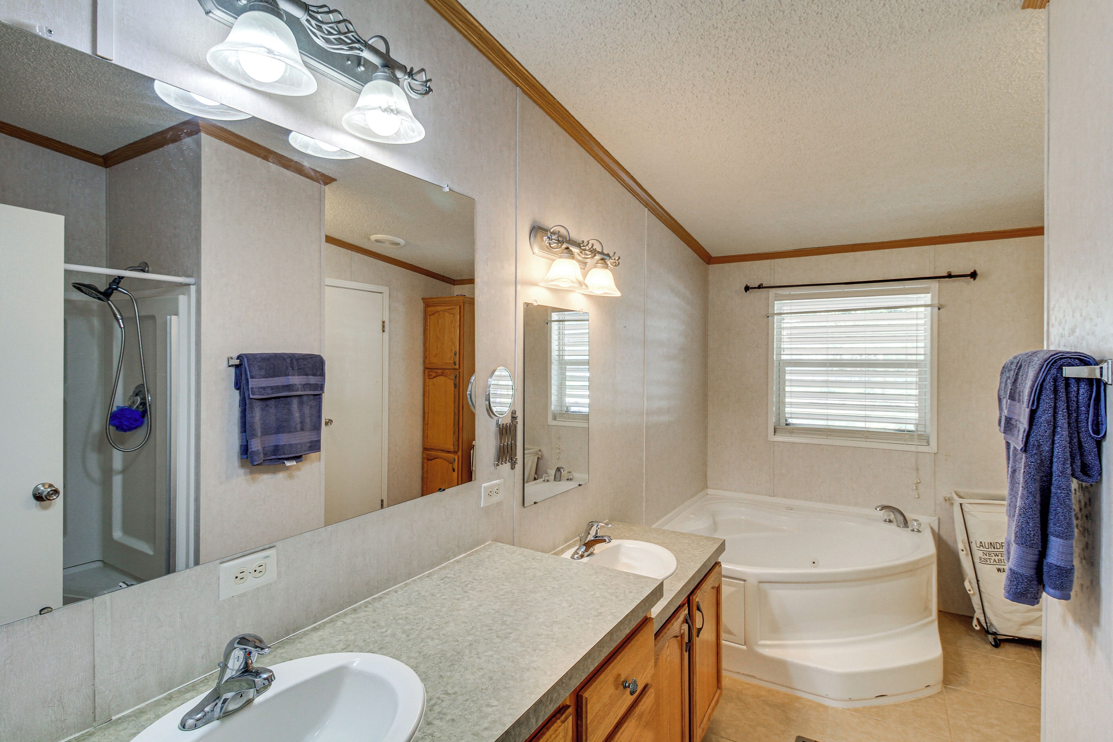 A bathroom with a double sink, a large mirror, a bathtub, and a window with blinds.