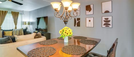 Un coin repas avec une table en bois, quatre chaises, un lustre et un vase rempli de tournesols.