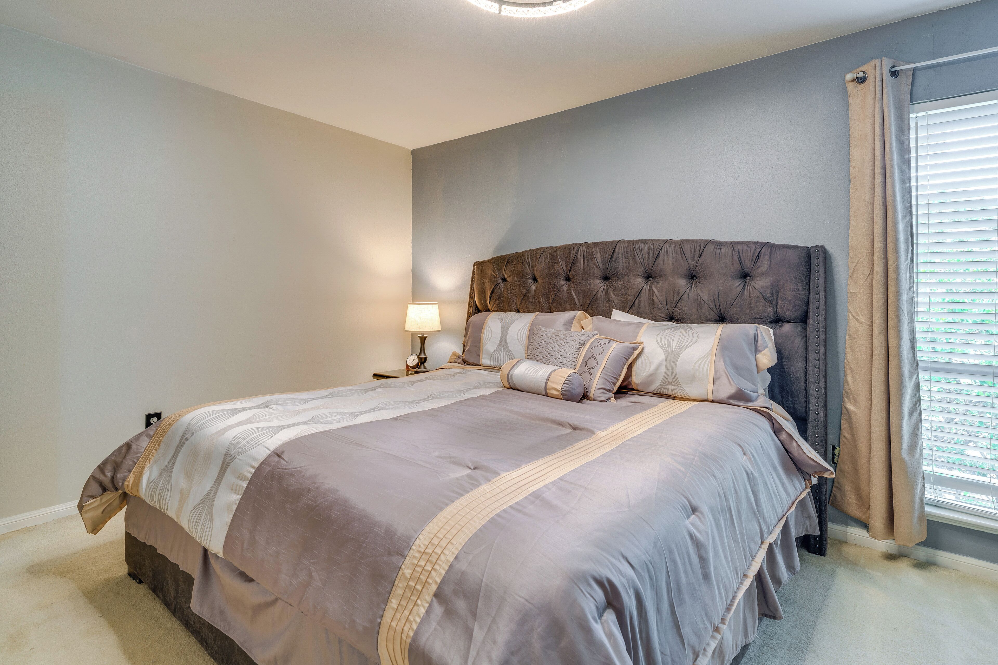 A bedroom with a large bed, a nightstand, a lamp, and a window with curtains.