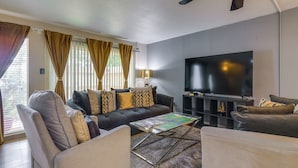 Een woonkamer met een bank, fauteuils, een salontafel, een flatscreen televisie en een boekenkast.