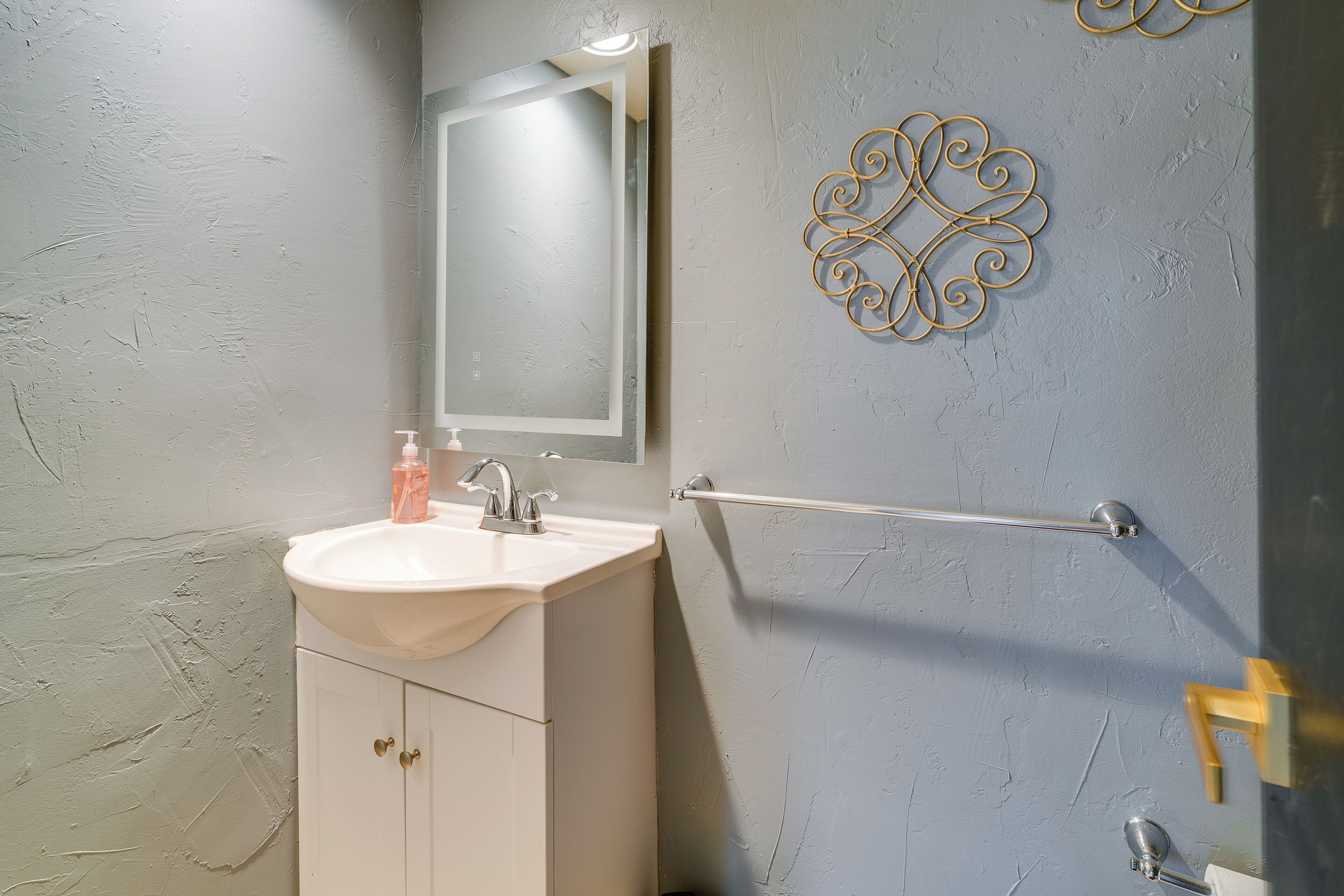 Een badkamer met een witte wasbak, een spiegel, een handdoekhouder en een decoratief wandobject.