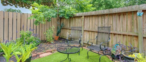A backyard with a wooden fence, a small lawn, and two metal chairs.