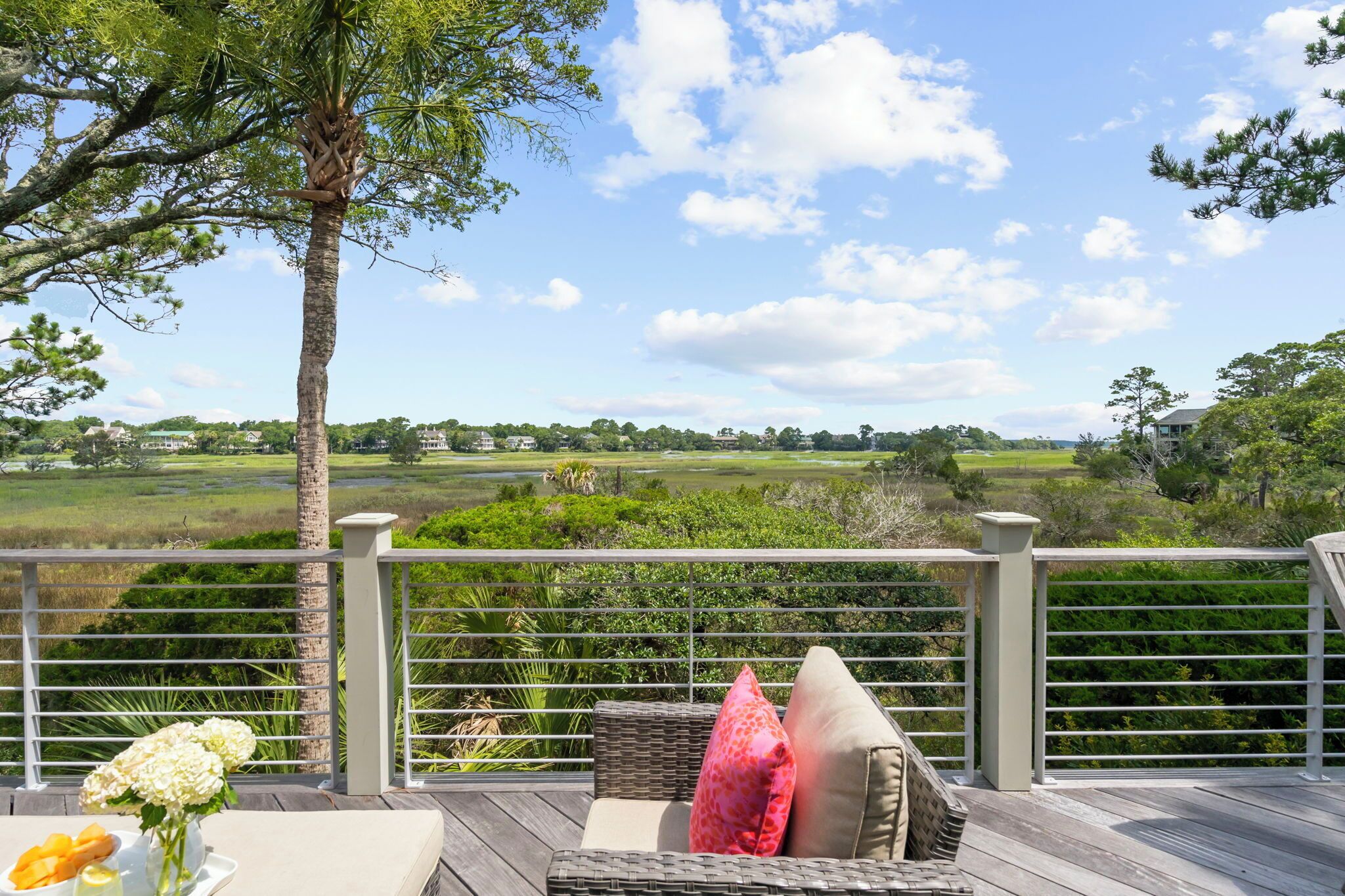 Una terraza con un sofá de mimbre, una mesa con flores y frutas, y vistas a un campo de golf.