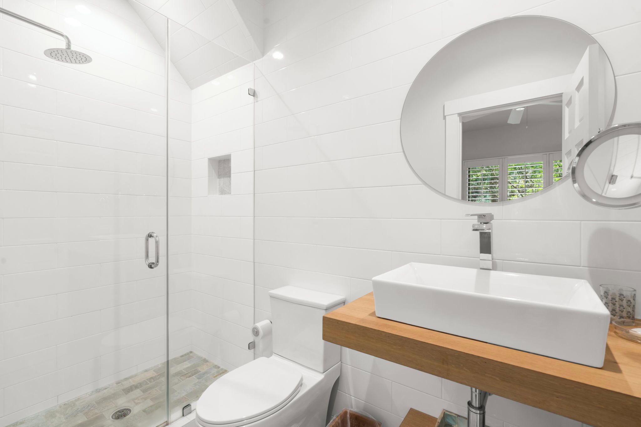 A modern bathroom with a glass-enclosed shower, a white toilet, and a wooden vanity with a large mirror.