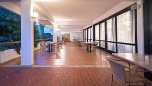 Un espacio interior amplio con varias mesas y sillas, ventanas grandes y piso de baldosas.