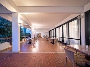 A spacious indoor area with multiple tables and chairs, large windows, and a brick floor. - Hotel Issa - Double Room Sea View 1 (Vis)