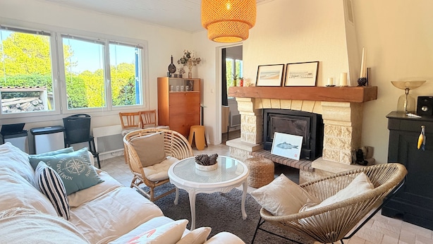 Een woonkamer met een open haard, rieten meubels, een ronde tafel en een boekenkast.