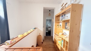 Een smalle gang met een houten bankje, een gevlochten mand en een houten wandplank met diverse spullen.