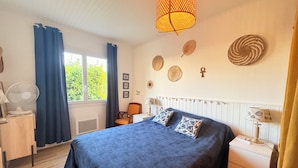 Een slaapkamer met een bed, nachtkastjes, een ventilator, gordijnen en een raam met uitzicht.
