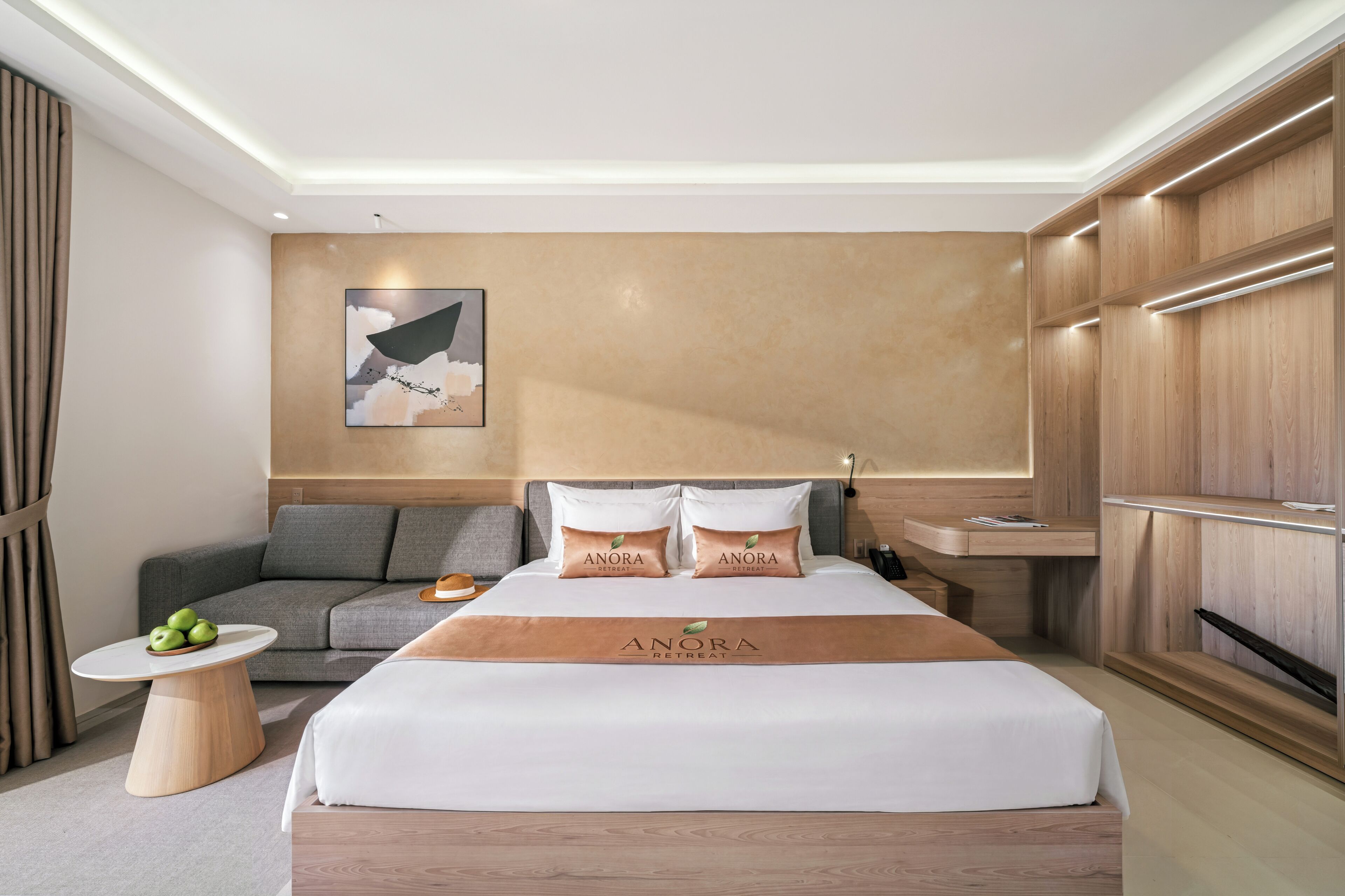 Een moderne hotelkamer met een bed, een bank, een klein tafeltje met appels, en een wanddecoratie.