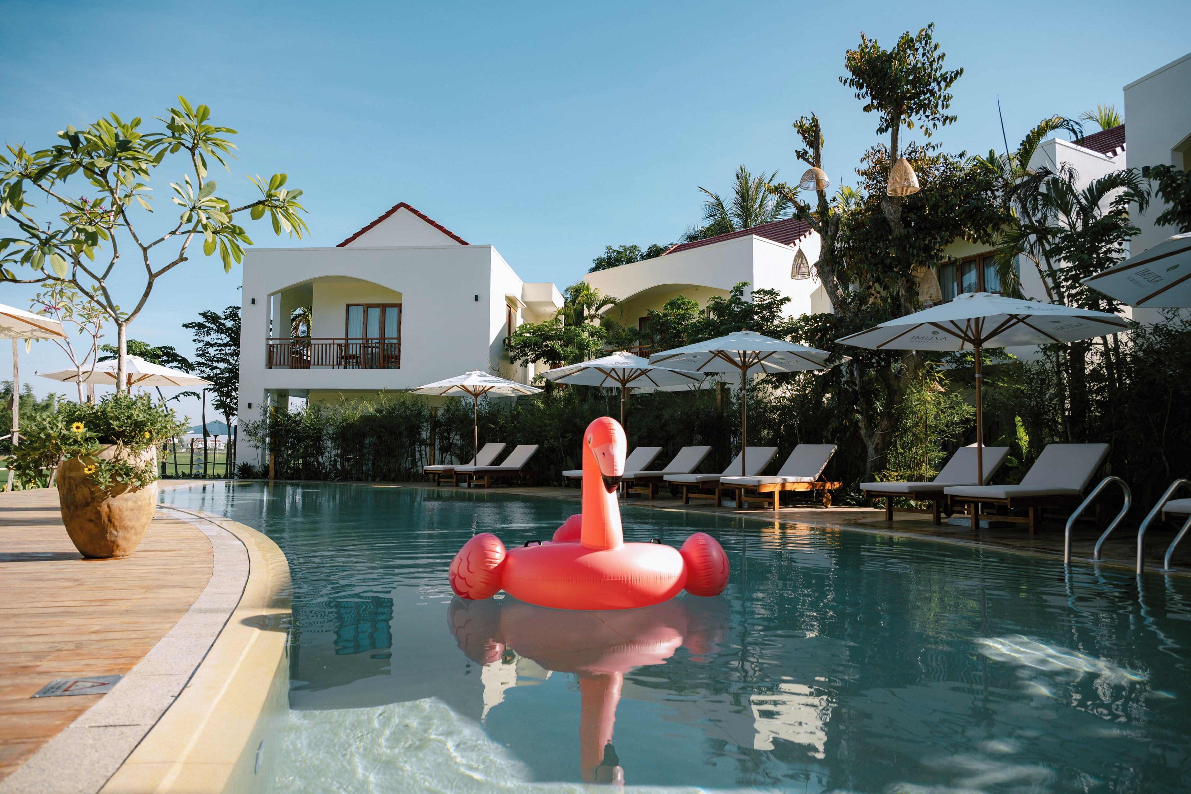 A pool area with lounge chairs, umbrellas, and a flamingo float.