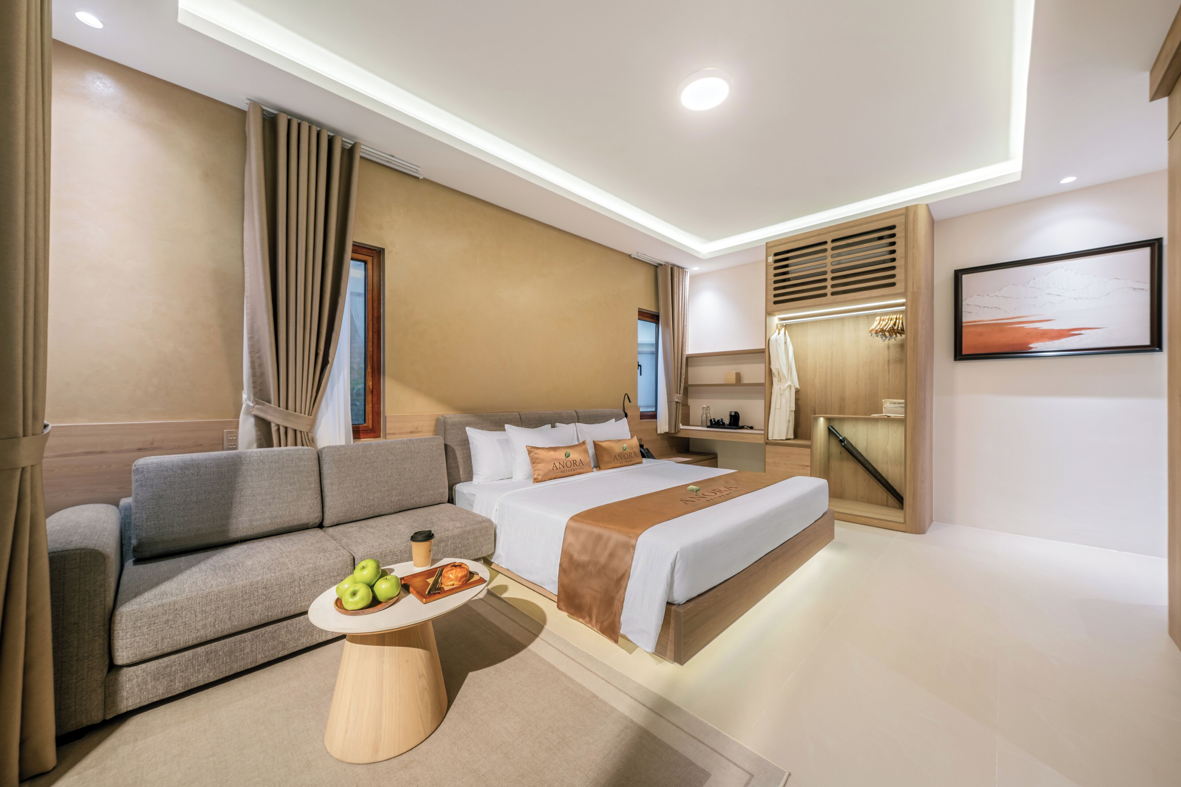 A modern hotel room with a bed, sofa, and a small table with apples.