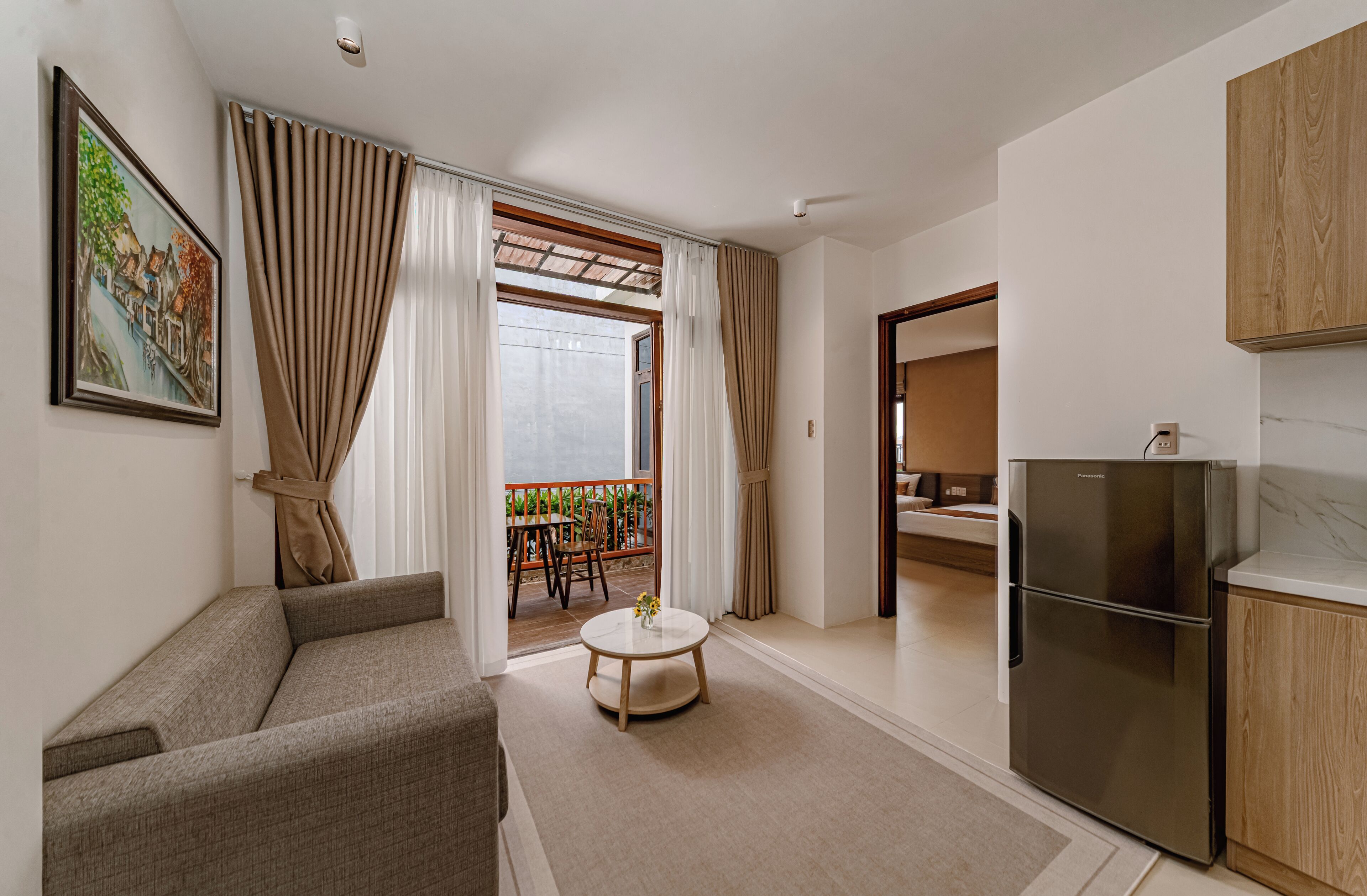 A modern living room with a sofa, a round coffee table, and a kitchen area with a refrigerator.