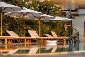 Zona junto a la piscina con sillones de descanso y sombrillas.