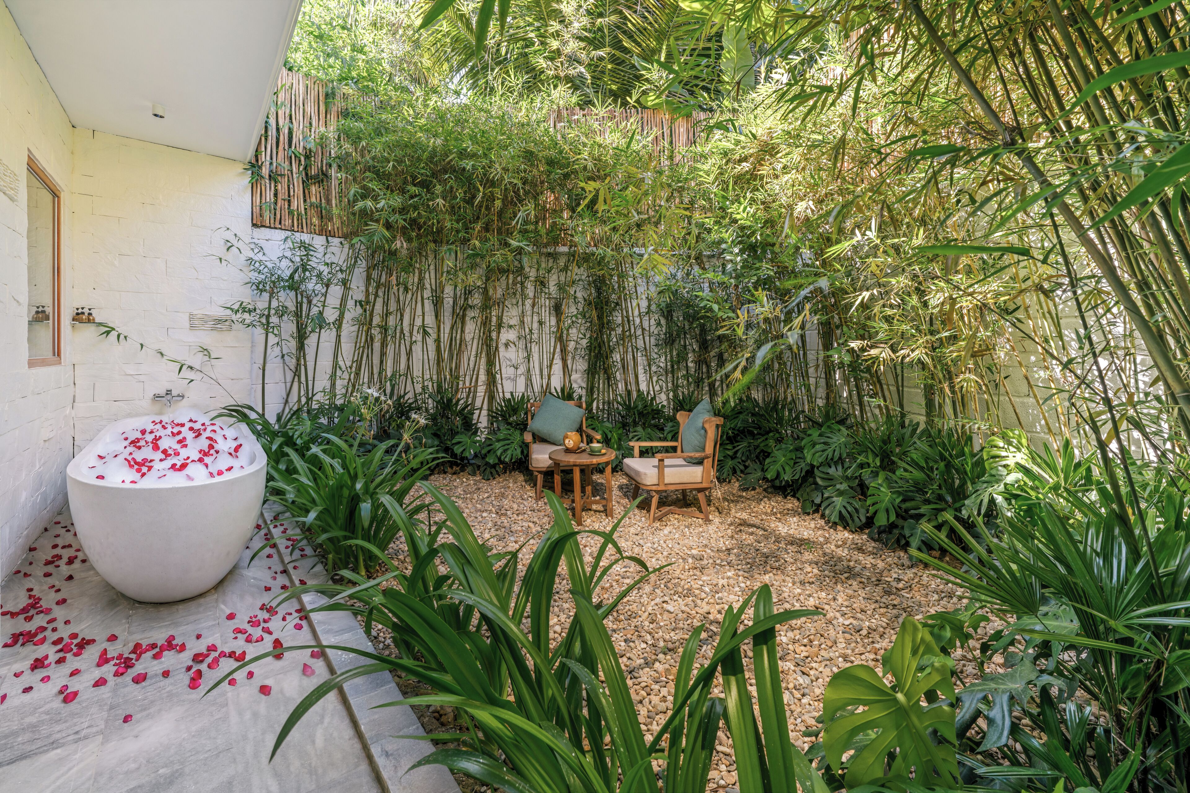 A garden with a seating area, a large planter, and a wall with a bamboo fence.
