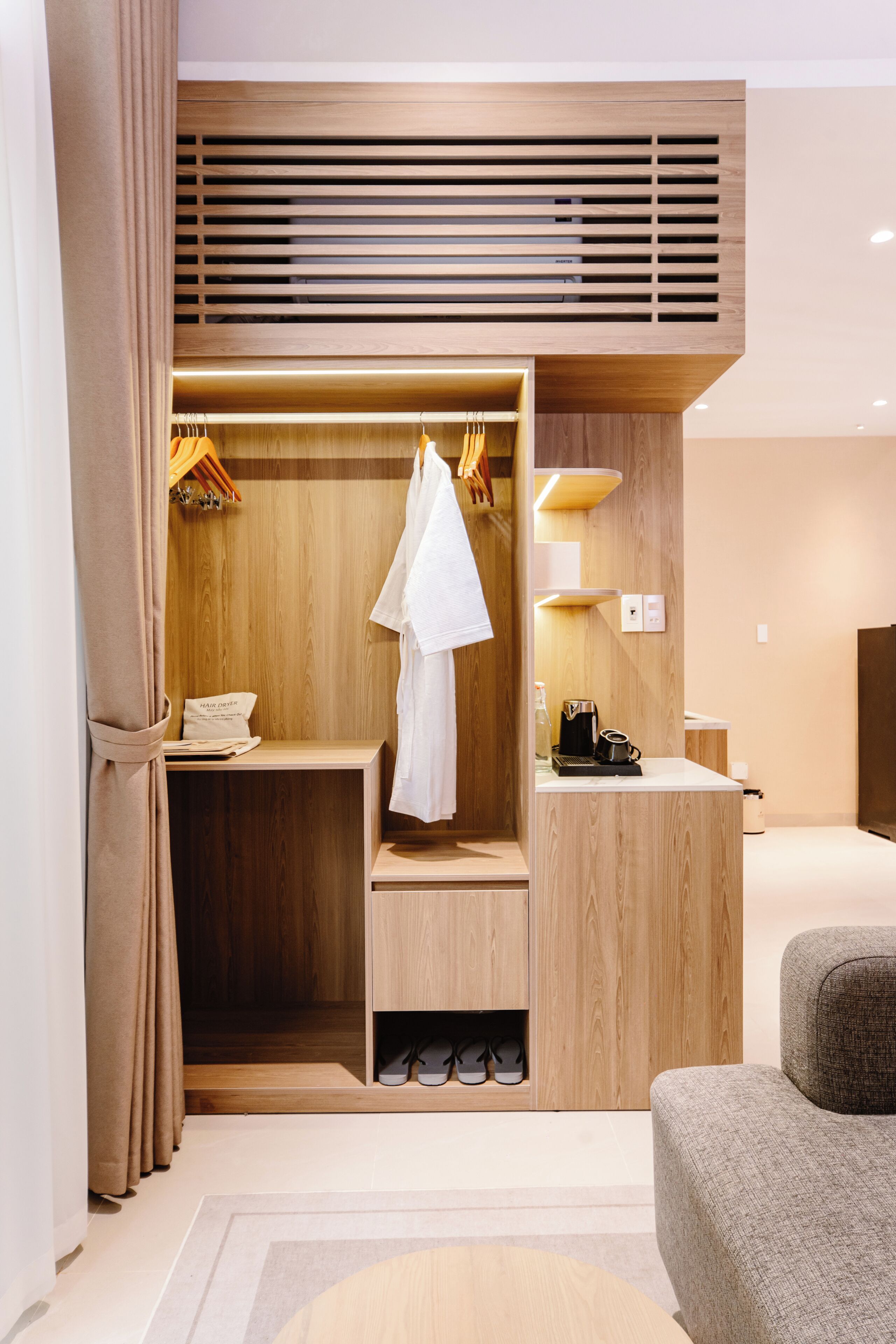 A modern hotel room with a wooden wardrobe, a seating area, and a small table with a coffee maker.
