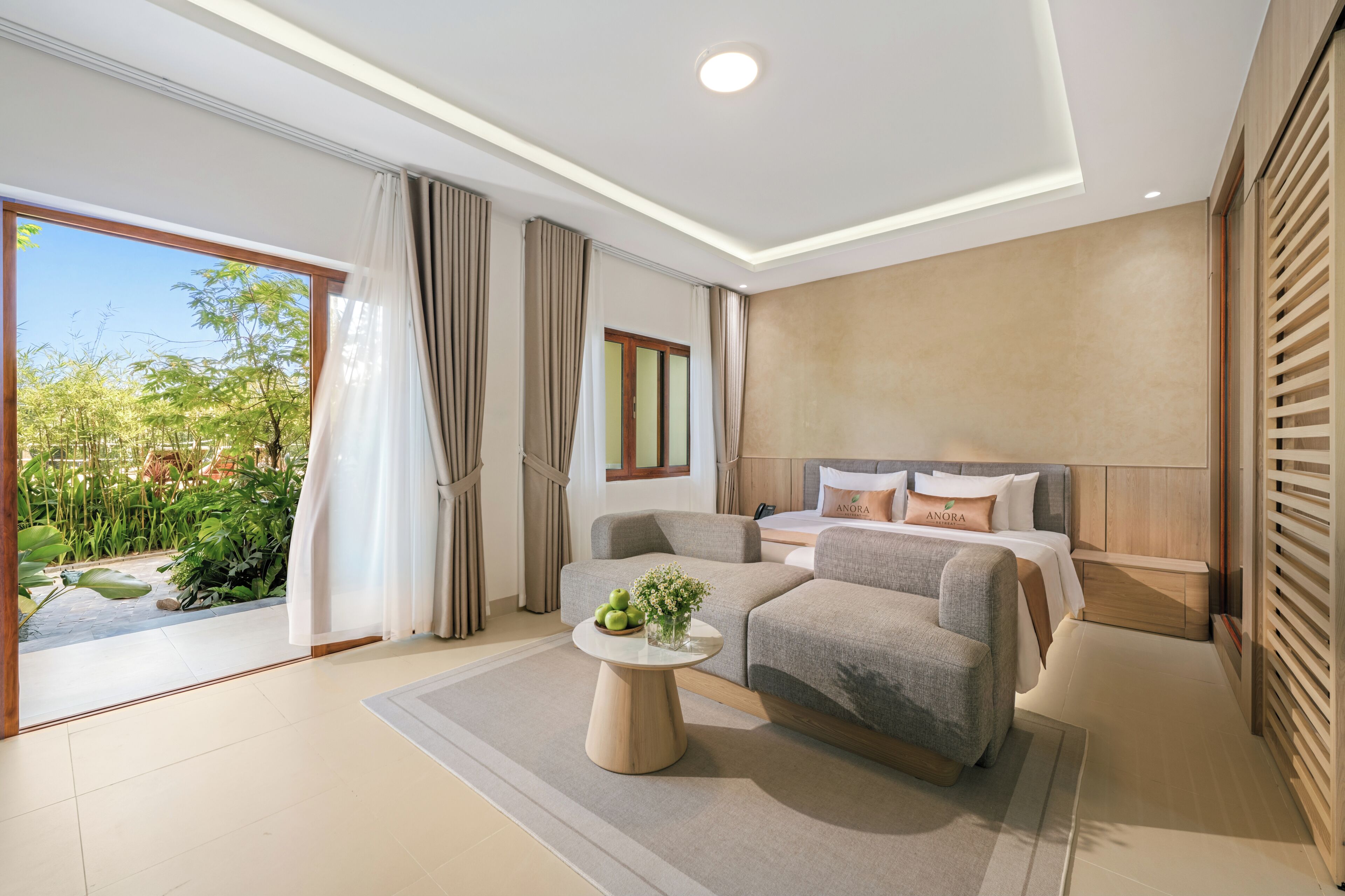 Una habitación de hotel moderna con un ventanal grande, un sofá, una cama y una pequeña mesa con fruta.