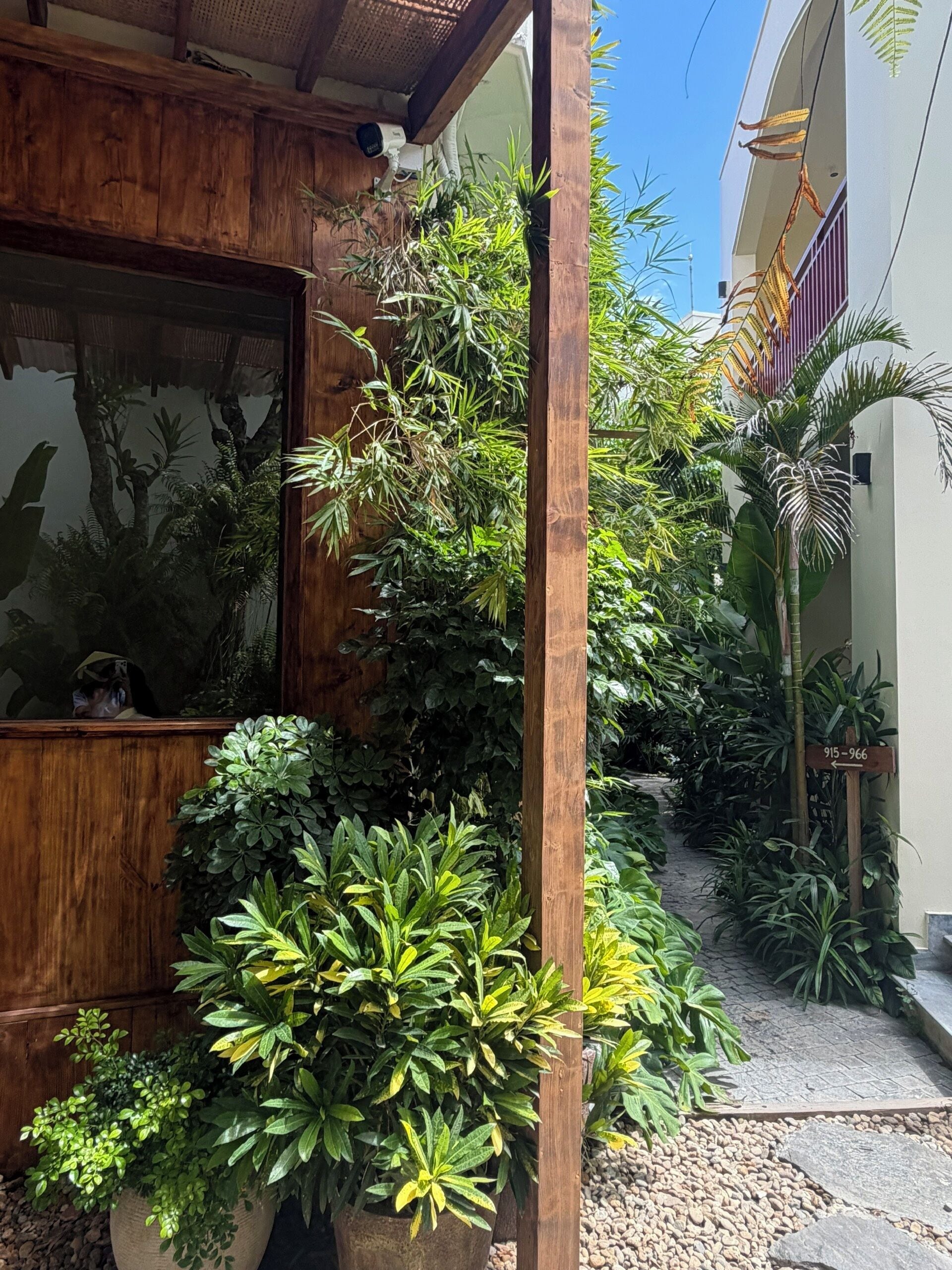 A wooden structure with a glass door, surrounded by lush greenery and a paved pathway.