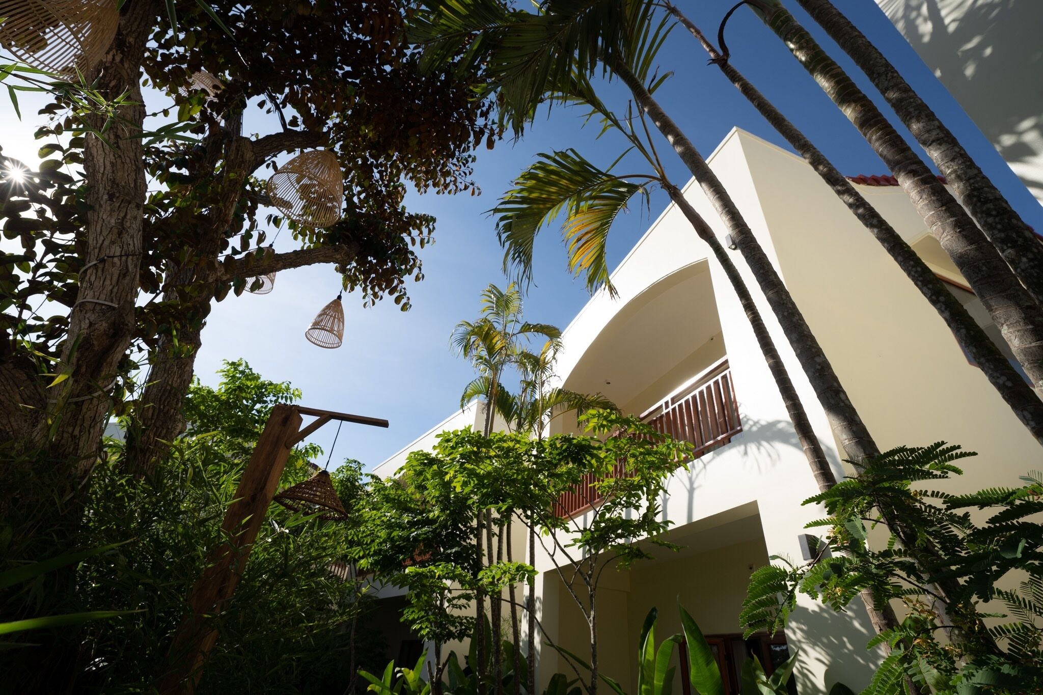 Un edificio con fachada blanca, un balcón y vegetación tropical circundante.