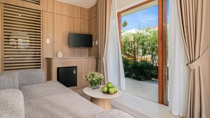 Un salon moderne avec un canapé, un téléviseur à écran plat, une petite table ornée de pommes et de fleurs, et une porte-fenêtre coulissante donnant sur un espace extérieur.